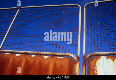 Detail of rusting aluminium gates topped with wire mesh with deep blue sky behind Stock Photo