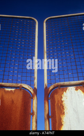 Detail of rusting aluminium gates topped with wire mesh with deep blue sky behind Stock Photo