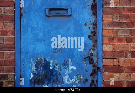 Door reinforced with sheet metal with weathered paint removed sign and rust-pitted yet still with handle letterbox and number 27 Stock Photo