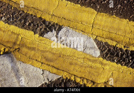 Detail of ragged-edged and cracked double yellow lines on slight curve and traversing white Give Way line Stock Photo