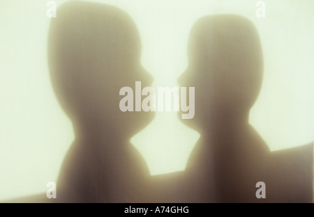 Shadow in warm light on pale cloth or curtain of two adult doll-like heads looking at or talking to or confronting each other Stock Photo