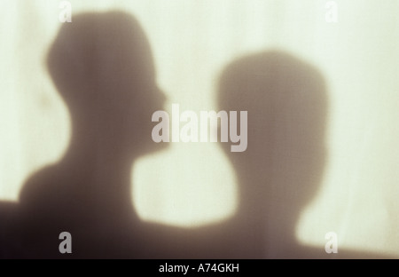 Shadow in warm light on pale cloth or curtain of two model adult heads in profile and facing viewer talking or watching Stock Photo