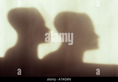 Shadow in warm light on pale cloth or curtain of two model adult heads in profile one behind other talking or watching Stock Photo