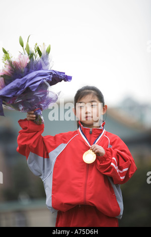 Young female athlete wearing gold medal and carrying flowers Stock Photo