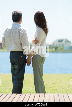 Couple standing and looking at lake, holding hands Stock Photo