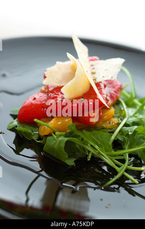 An antipasto selection of mixed roast peppers on a bed of rocket with parmesan shavings served on a black plate Stock Photo