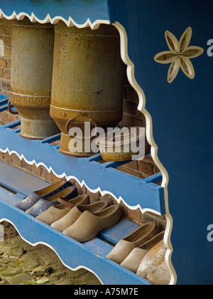 Blue and white wooden rack outside a historic farmhouse with clogs and two milk cans churns Stock Photo