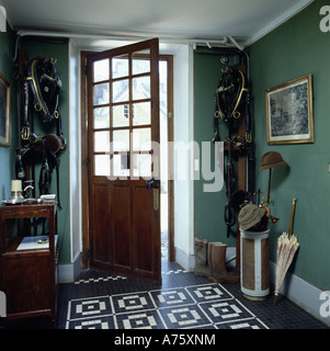 Tiled floor in green hall with horse bridle on wall and open half-glazed door Stock Photo