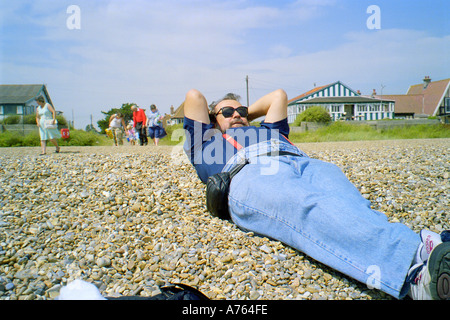 A Man laying down on the beach in Thorpeness Suffolk England Stock Photo