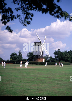 Village green cricket match bowler batsman & fielders in Iconic English idyllic quintessential Mountnessing Post Mill Brentwood Essex countryside UK Stock Photo