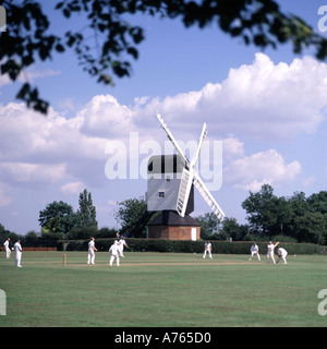 Iconic quintessential England idyllic village green cricket match bowler batsman & fielders Mountnessing Post Mill beyond in Essex countryside UK Stock Photo