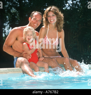 young couple with daughter sitting by swimming pool Stock Photo