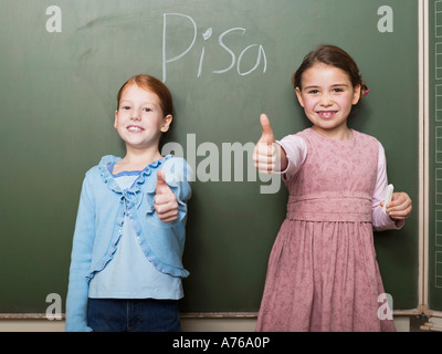 Girls (4-7) standing by blackboard, showing thumbs up sign Stock Photo