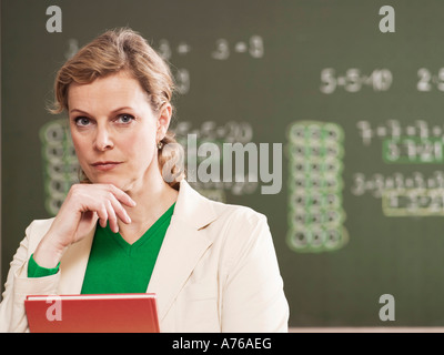 Woman standing by blackboard, holding book, close-up, portrait Stock Photo