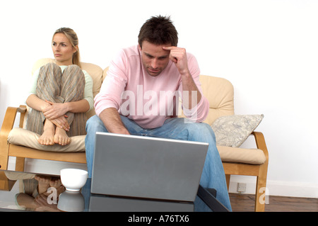 couple sitting on a sofa man looking at a laptop computer with woman looking bored Stock Photo