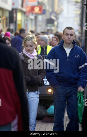 young people walking in front of motorised street cleaner in crowds out christmas shopping in Belfast Christmas Eve Stock Photo
