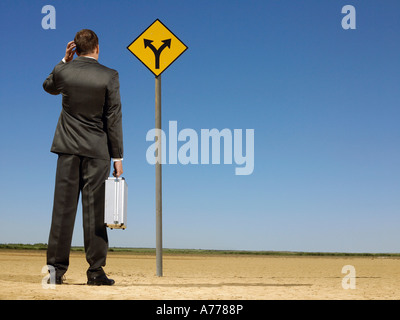 Rear view of confused businessman looking at desert road sign Stock Photo