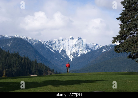 Man walking toward edge of Capilano reservoir North Vancouver British Columbia Canada snow capped two Lions in background Stock Photo