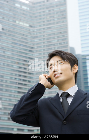 Young businessman using cell phone, looking away, office building in background Stock Photo