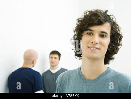 Young man smiling at camera, two young men talking in background Stock Photo