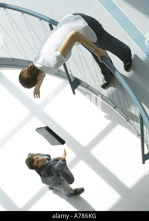 Businessman throwing briefcase up to woman from lower floor, full length, high angle view Stock Photo