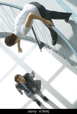 Businessman holding cell phone up to woman from lower floor, full length, high angle view Stock Photo