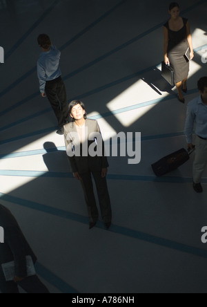Businesswoman standing with eyes closed in ray of sunlight while people pass by