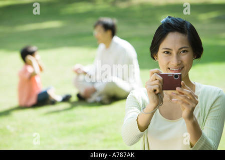 Woman aiming digital camera, smiling at camera Stock Photo