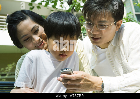 Boy with mother and father, father holding out cell phone for boy to see Stock Photo