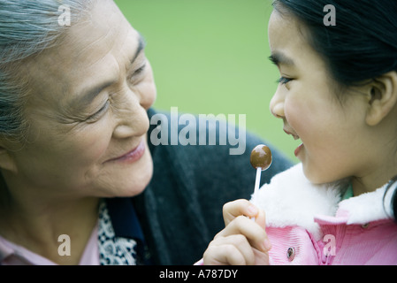 Girl eating lollipop, looking at grandmother, close-up Stock Photo