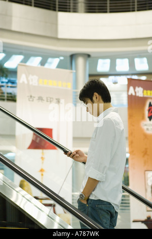 Man on escalator checking cell phone Stock Photo