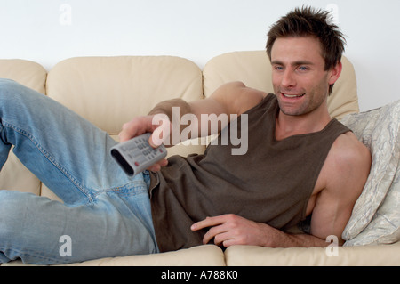 man laying on a sofa watching television changing channels with a TV remote zapper Stock Photo