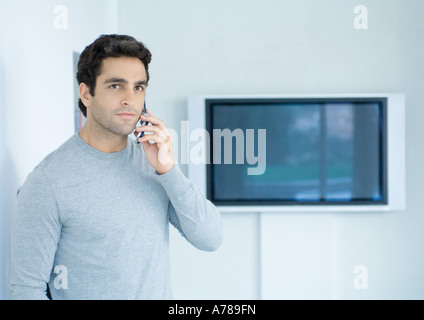 Man using cell phone, widescreen TV in background Stock Photo
