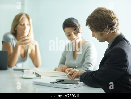 Mature man sitting at table with teenage girl and young female professional, signing document Stock Photo