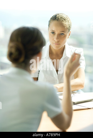 Two young female professionals sitting across from each other, having conversation, focus on woman listening in background Stock Photo