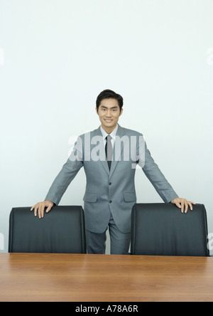 Businessman standing in conference room with hands on backs of chairs, portrait Stock Photo