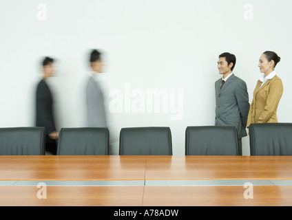 Business executives standing, facing associates arriving in conference room Stock Photo