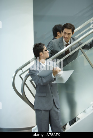 Businessman standing on stairs, looking down at file held by associate Stock Photo