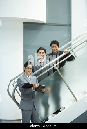 Three businessmen, two standing on stairs, smiling at camera Stock Photo