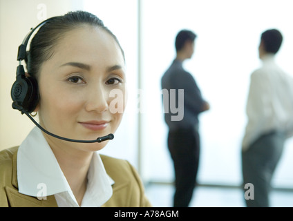 Businesswoman wearing headset, colleagues standing in background, portrait Stock Photo