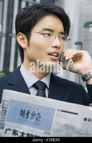 Businessman holding Chinese newspaper, using cell phone Stock Photo