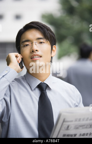 Businessman with newspaper using cell phone, looking at camera Stock Photo