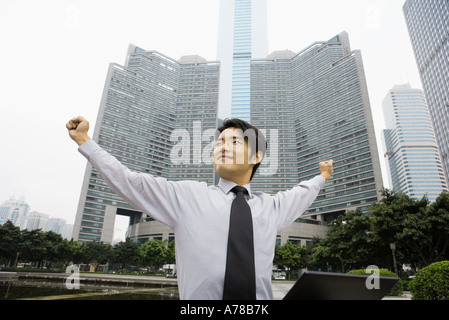 Businessman standing with arms out, skyscraper in background, low angle view Stock Photo