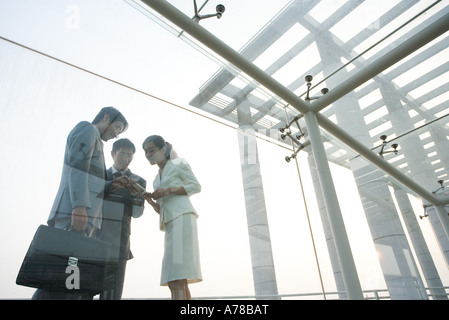 Three business executives standing in glass walkway, talking, low angle view Stock Photo