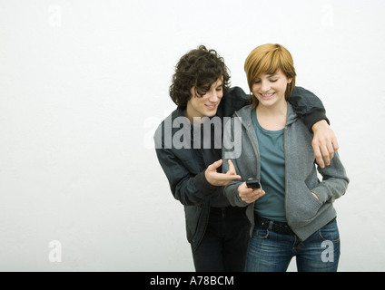 Young adult couple, man with arm around woman, woman holding cell phone Stock Photo