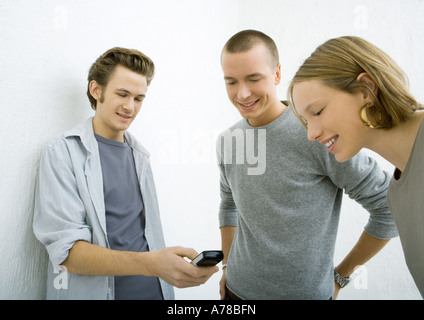 Three young friends looking at cell phone, smiling Stock Photo