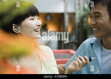 Young couple sharing earphones, laughing Stock Photo