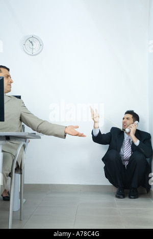 Businessman sitting in corner, using telephone, arguing with colleague in foreground Stock Photo