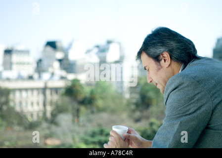 Businessman holding cup, city in background Stock Photo