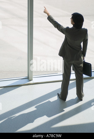 Businesswoman standing by window, pointing to distance, high angle view Stock Photo